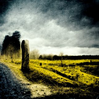 A tall standing stone beside a faint path in a desolate field under a darkening storm.