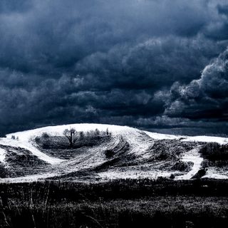 A snow-domed burial mound topped by one bare tree beneath a black storm.