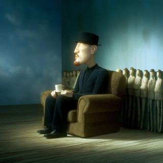 A man seated among pale carved statues in a dim room, as if taking tea with the stone figures.