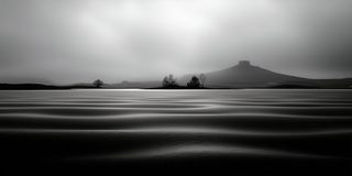A vast expanse of smooth pale sand under a low misty sky, a flat-topped hill faint on the far shore.