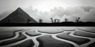 A dark pyramid mountain over a shore where bright channels of water thread through wet sand.