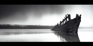 The bare ribs of a wrecked boat rising from misty shallow water.