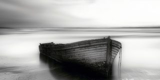An old derelict boat hull resting on still water below mountains.