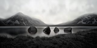 Stones gathered in still water at the foot of a misty mountain.