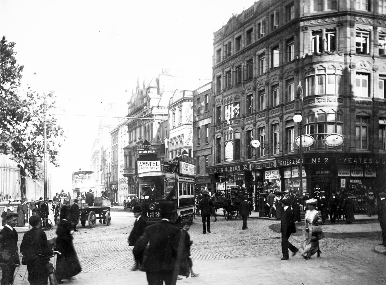 Black-and-white view across Nassau Street with electric trams, tracks, pedestrians, bicycles, and horse-drawn traffic, photographed between 1897 and 1904.