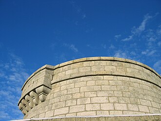 coursed granite ashlar rising to a projecting string course and a parapet, sky behind, no other structure in the frame
