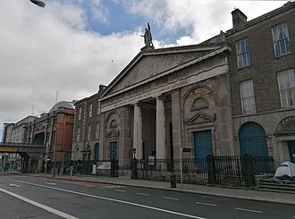 a columned church portico on the right, a long brick terrace running away to the left, an iron railway bridge and a curved station roof beyond
