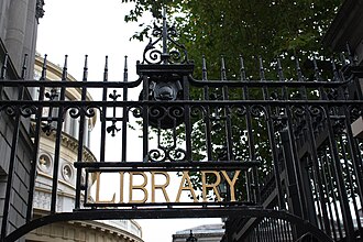 a tall iron forecourt gate with gilt lettering worked into it, a columned stone portico standing behind