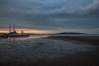 a broad tidal flat running out to still water, two tall banded chimneys standing on the far shore, low cloud above