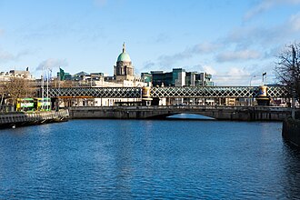 a wide reach of river between stone quay walls, a low road bridge crossing in the foreground, a girder railway viaduct behind it